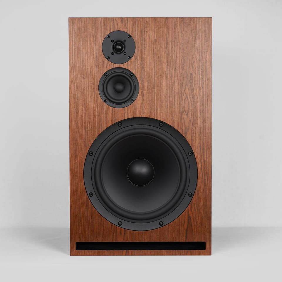 Gema three-way loudspeaker in wood veneer, front view: dome tweeter, small midrange, large woofer, slot port below.