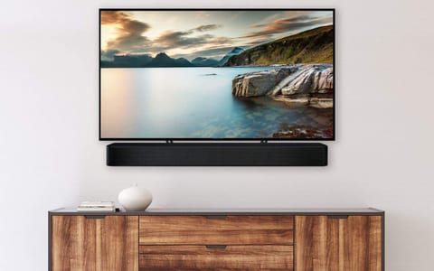 Wall-mounted flat-screen TV showing a coastal landscape, with a black soundbar below on a wooden sideboard.