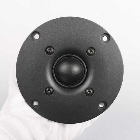 SB26STAC-C000-4 tweeter held in a white-gloved hand: a soft textile dome in the centre of a black textured round faceplate with four bolt holes.