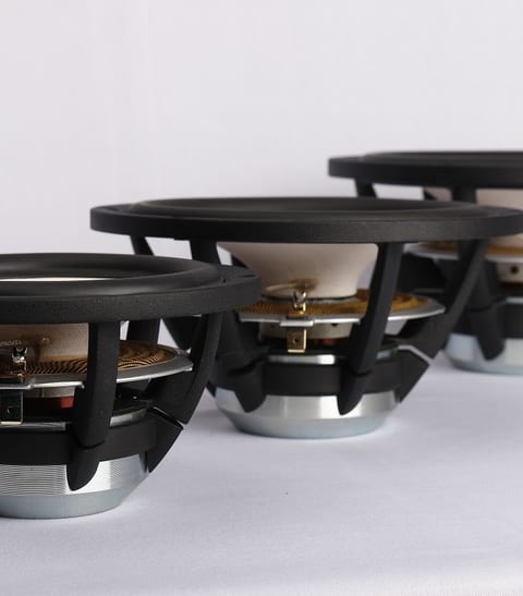 Three cone drivers on a white surface seen from behind, showing black cast baskets, spiders and metal motor assemblies.