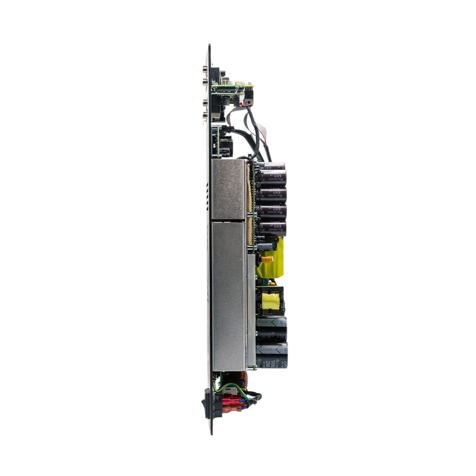 The same FA503 seen edge-on, showing how much sits behind the plate: two long heatsink blocks, banks of electrolytic capacitors, a switch-mode power supply and the input board, all stacked within roughly a hand's depth.