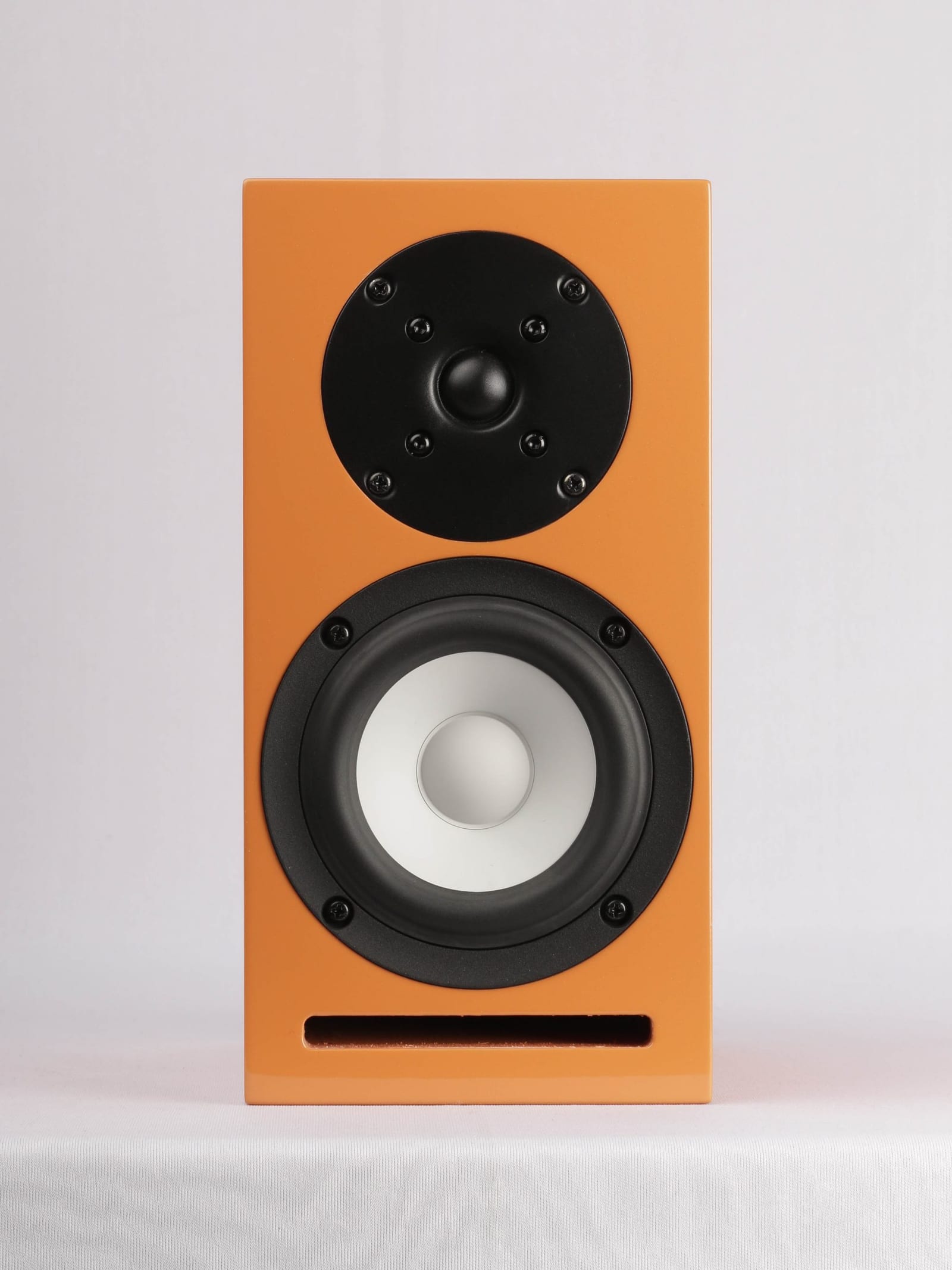 Micro-C bookshelf speaker in orange gloss, straight on: a black soft dome tweeter above a 4-inch white ceramic cone midwoofer, with a slot port across the bottom of the baffle.