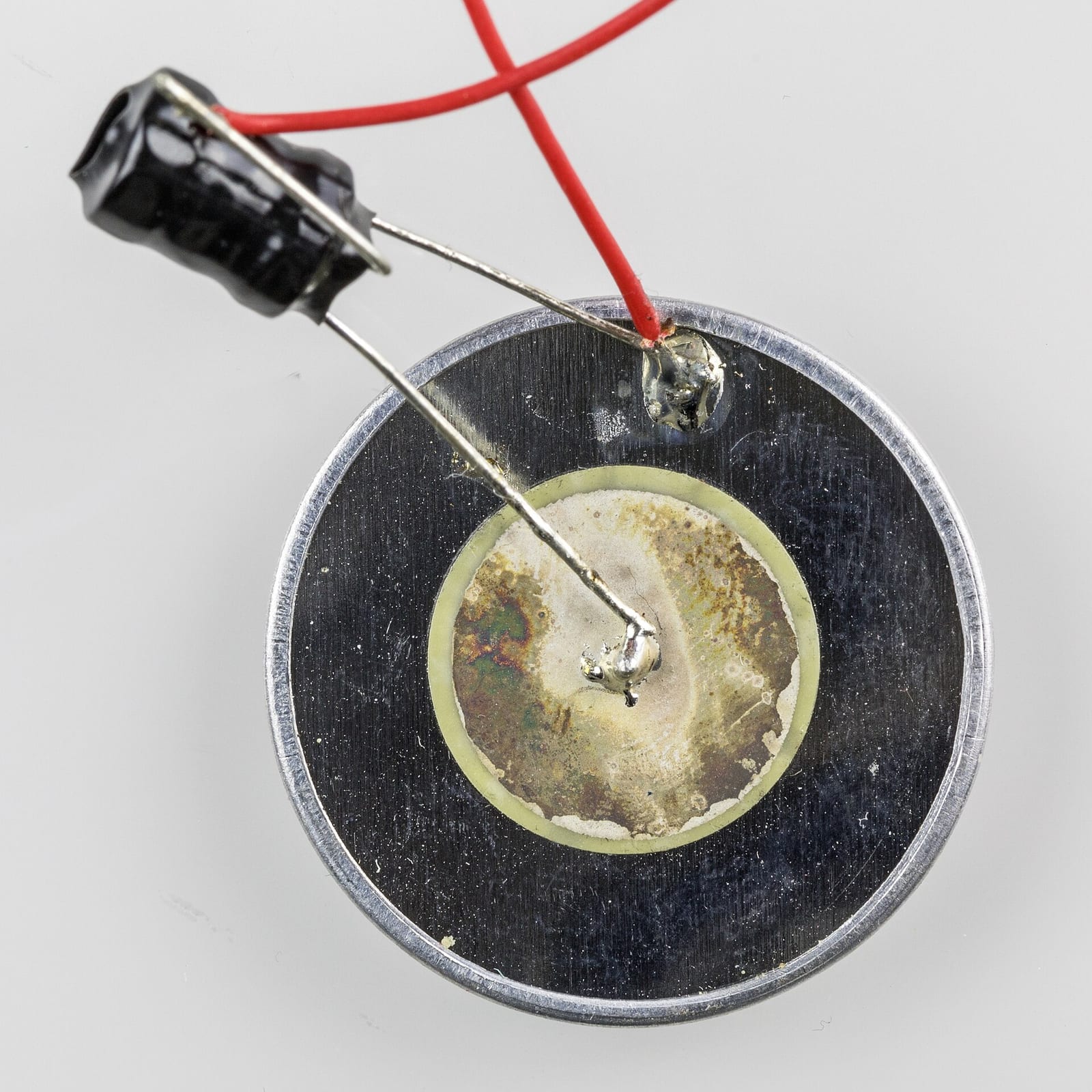 Close-up of a piezoelectric disc element: a round metal diaphragm with a yellow-rimmed ceramic disc bonded to its centre and two soldered lead wires.