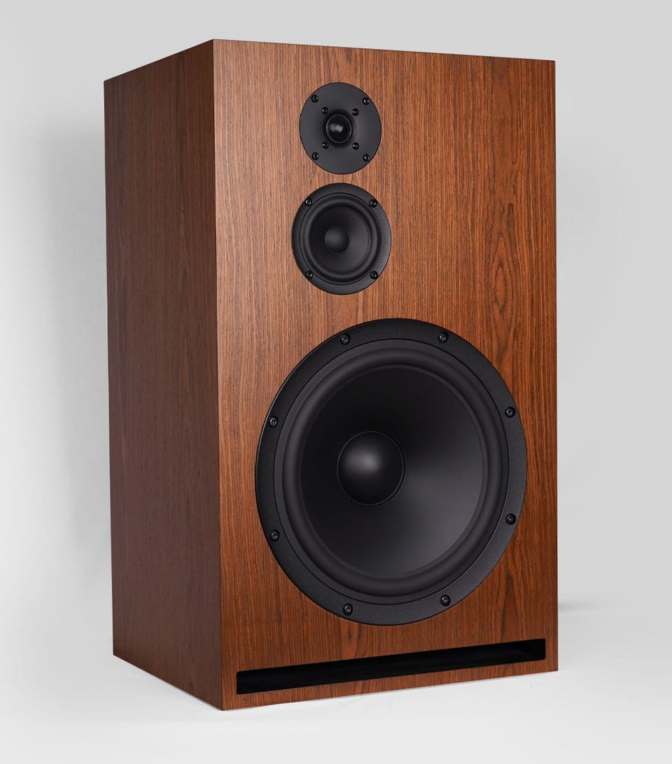 Gema three-way speaker in wood veneer, angled view: dome tweeter, small midrange, large woofer, slot port below.