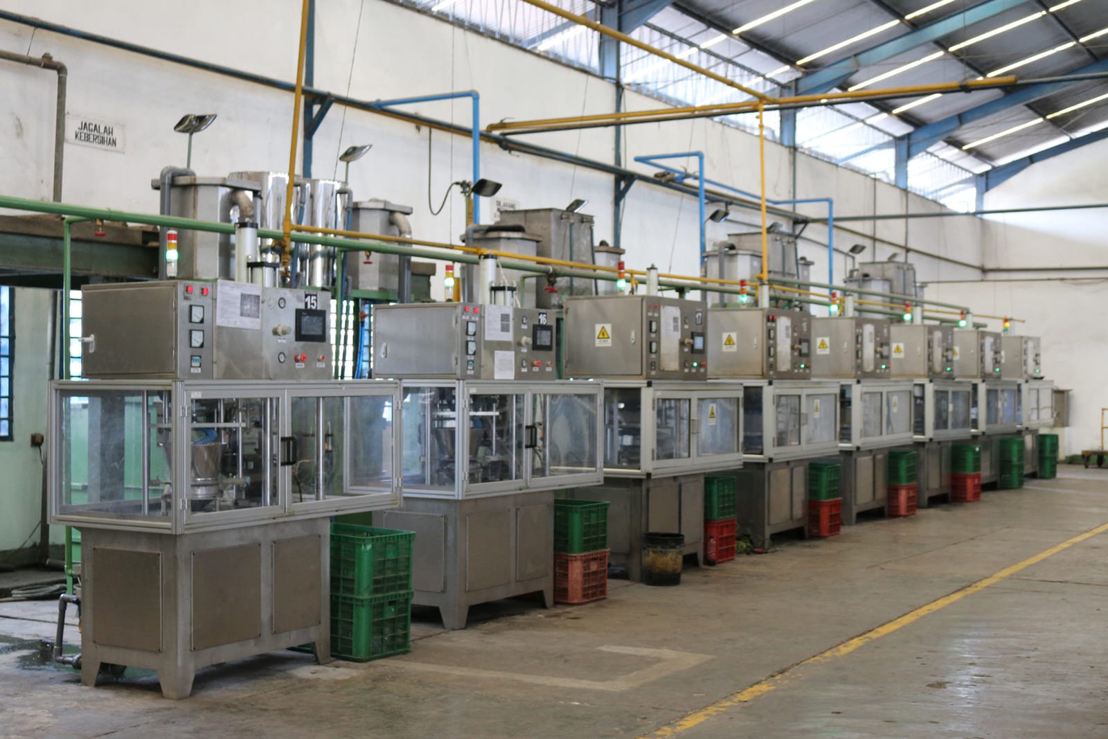 A long line of identical press stations running the length of a factory hall, each with its own control panel and green feedstock drum.
