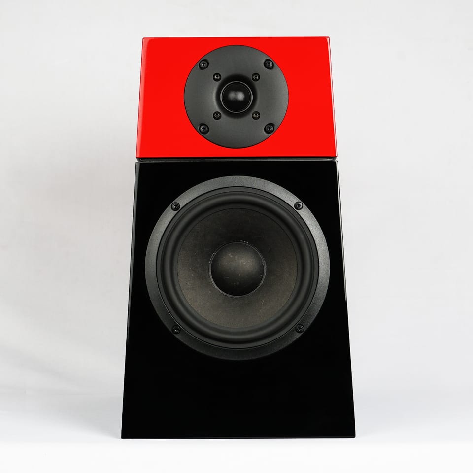 Tifa 6 standmount straight on: a red gloss upper module carrying a 26 mm fabric dome above a black gloss lower cabinet holding a 6-inch natural-fibre cone midwoofer, the whole baffle raked forward.